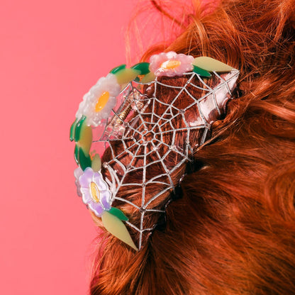 close up of a clear spiderweb and flower hair claw clip in red hair updo with pink background