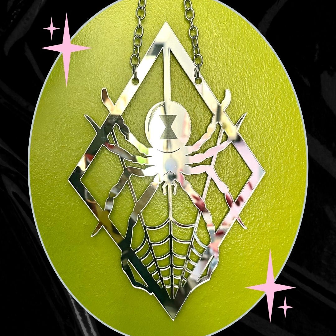 Metallic spider web pendant on a green circular background with decorative stars.