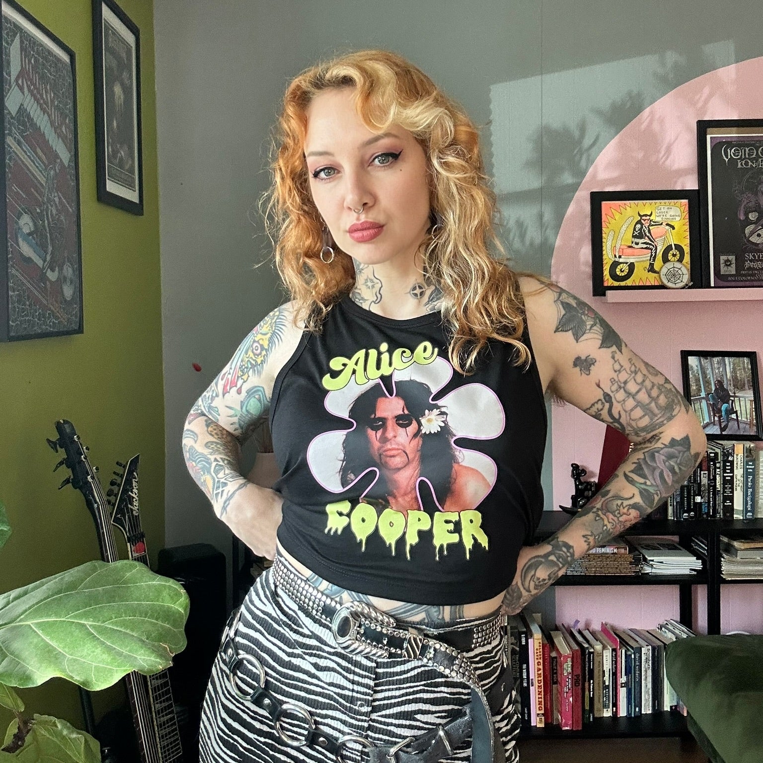 Person wearing a black tank top with graphic design in a room with books and decor.