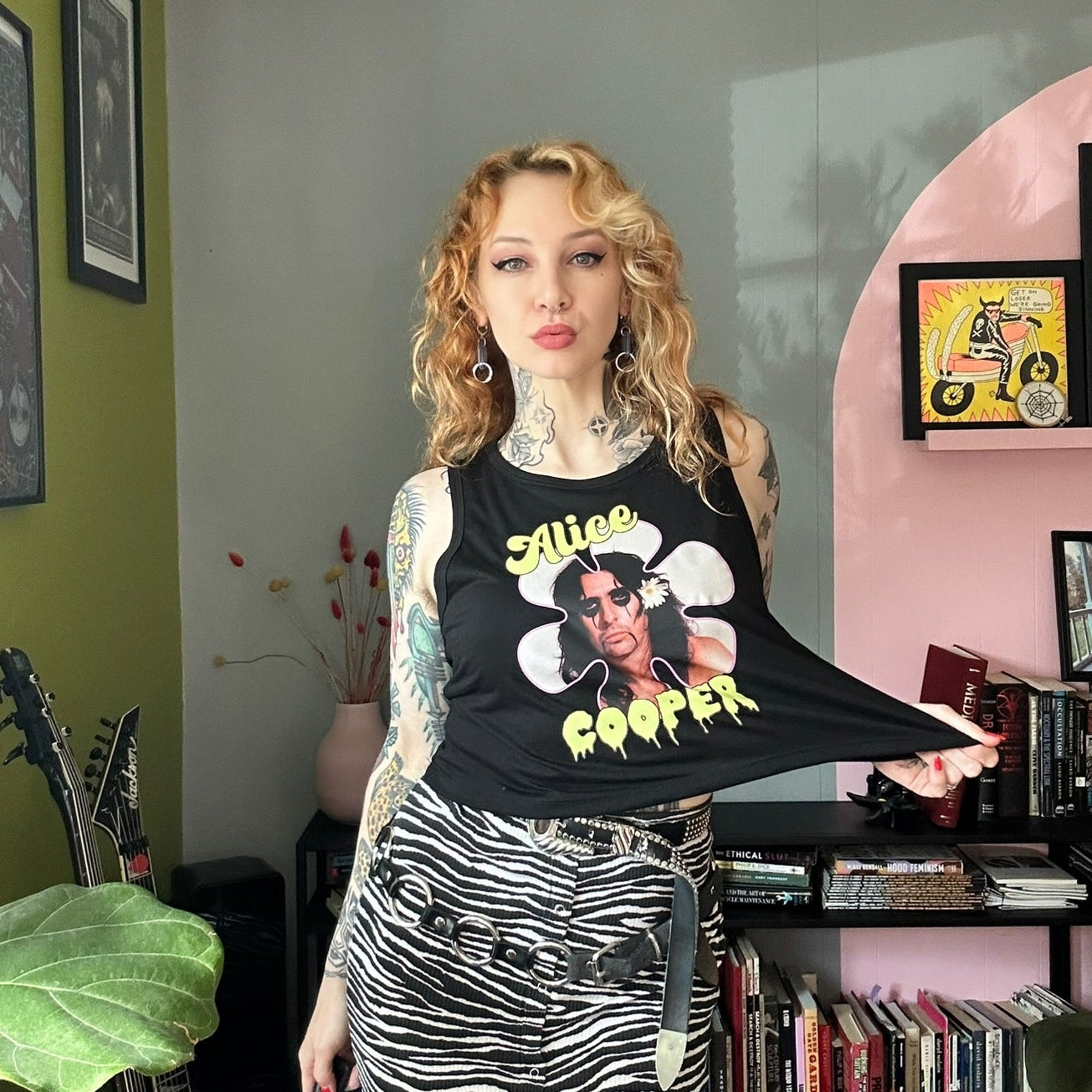 Woman wearing a black tank top with graphic design in a room with books and decor.