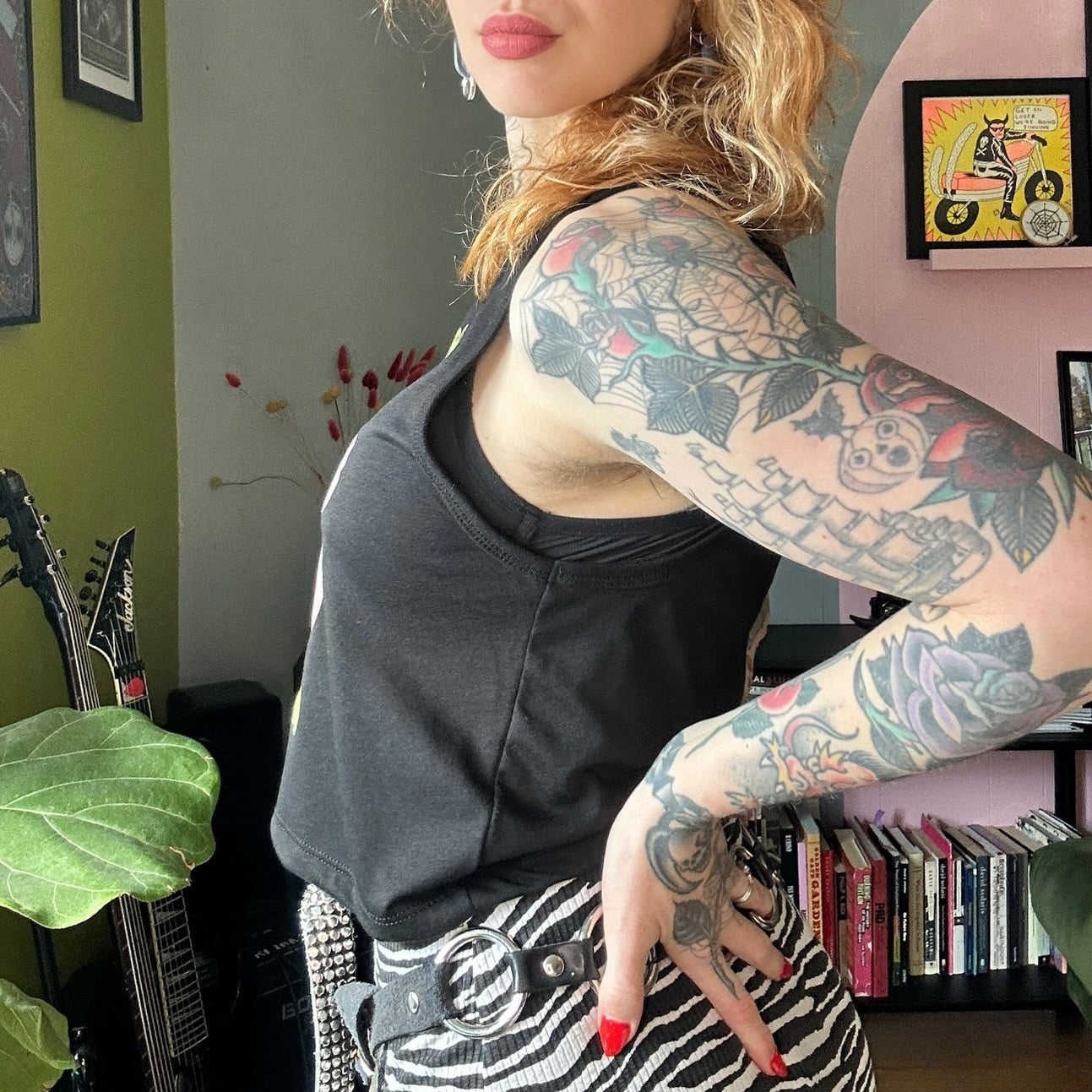 Woman with tattoos standing in a room with green walls and a pink shelf.