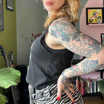 Woman with tattoos standing in a room with green walls and a pink shelf.
