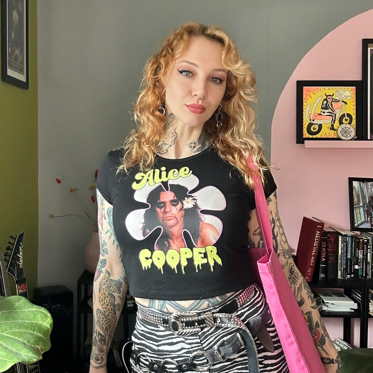 Person wearing a black t-shirt with graphic design in a room with green walls and a pink arch.
