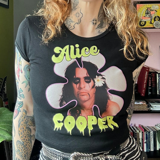 Person wearing a black t-shirt with Alice Cooper design in a room with books and decor.