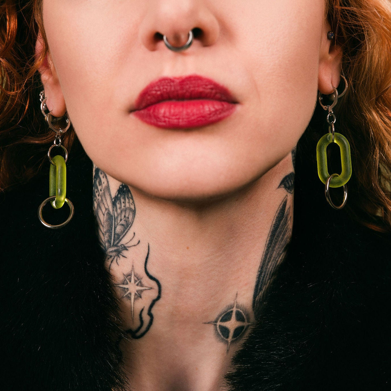Close-up of a person with tattoos and green earrings against a green background