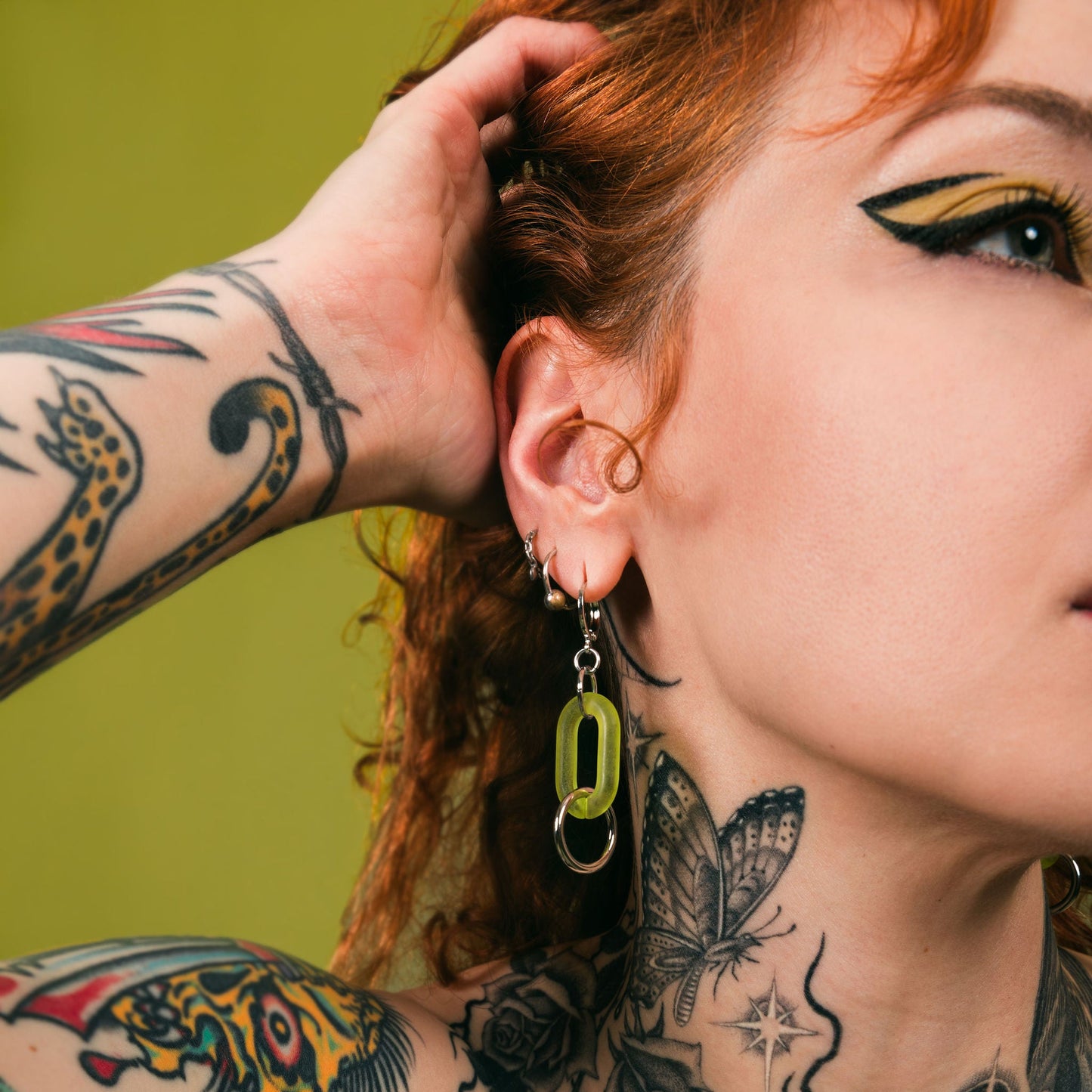 Person with tattoos and necklaces against a green background