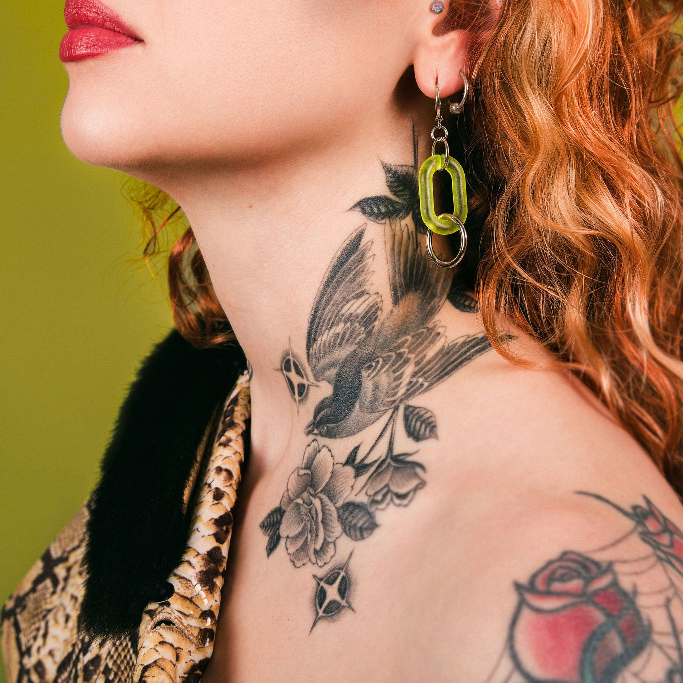 Person with tattoos on neck and shoulder against a green background