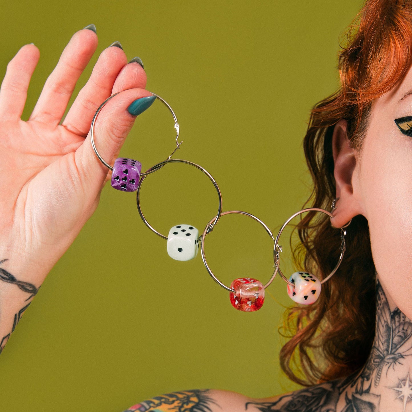 Person wearing hoop earrings with dice charms against a green background