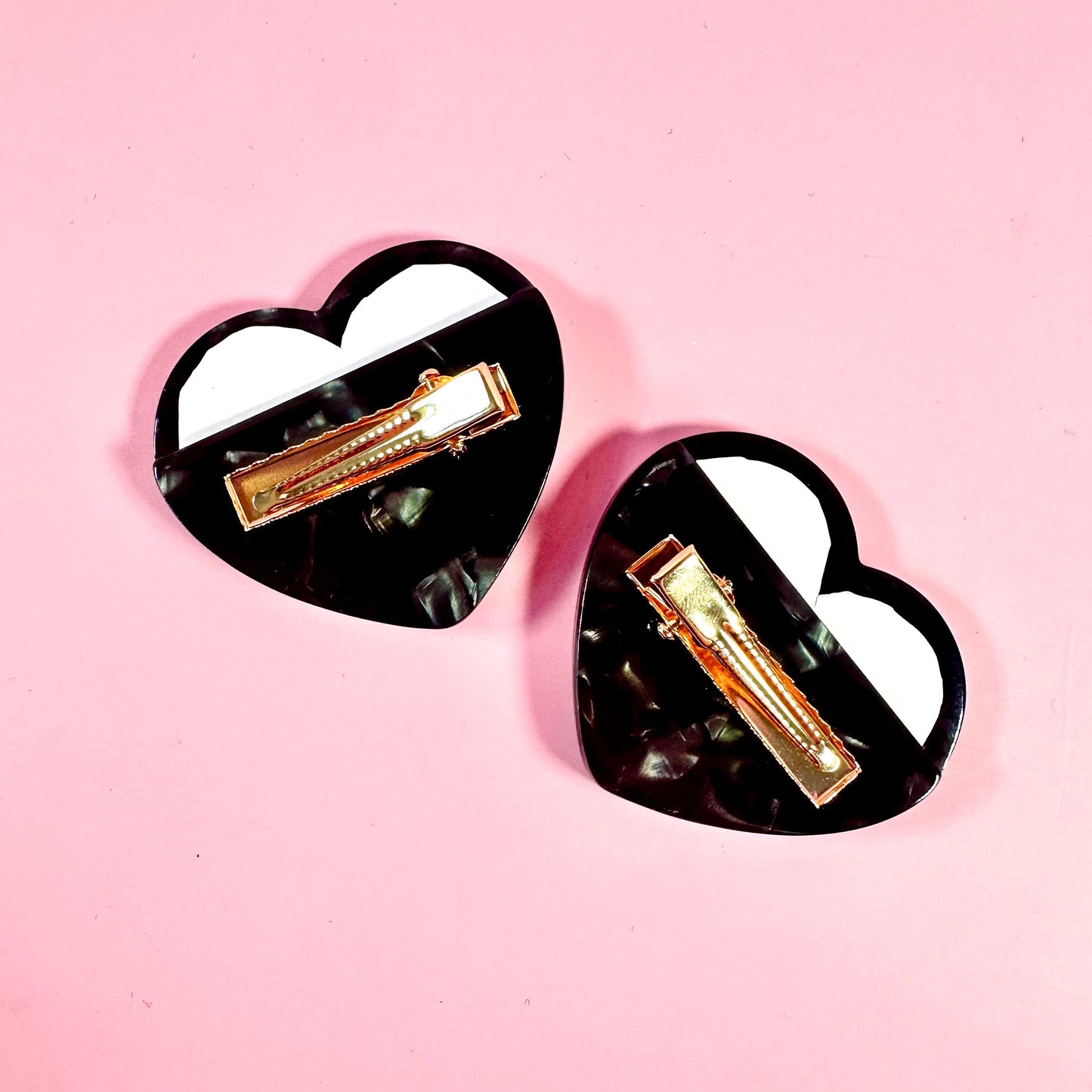 Heart-shaped hair clips with gold accents on a pink background