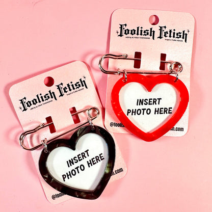 Two heart-shaped keychains on Foolish Fetish cards against a pink background