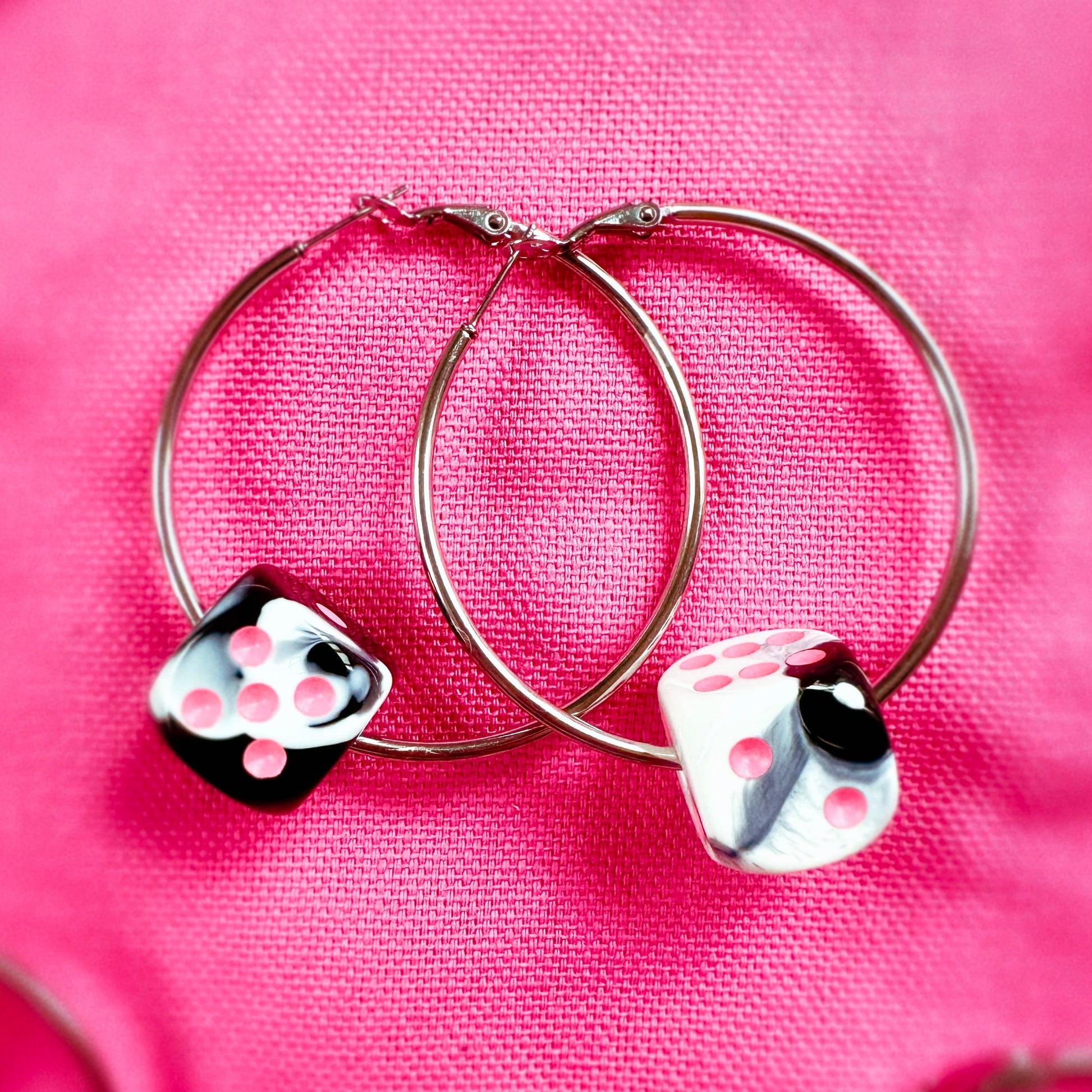Hoop earrings with dice charms on a pink fabric background