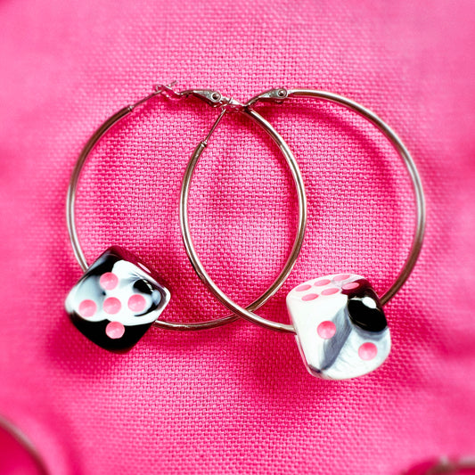 Hoop earrings with dice charms on a pink fabric background