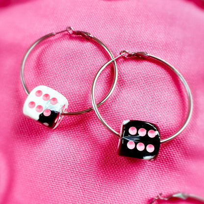 Hoop earrings with dice charms on a pink fabric background