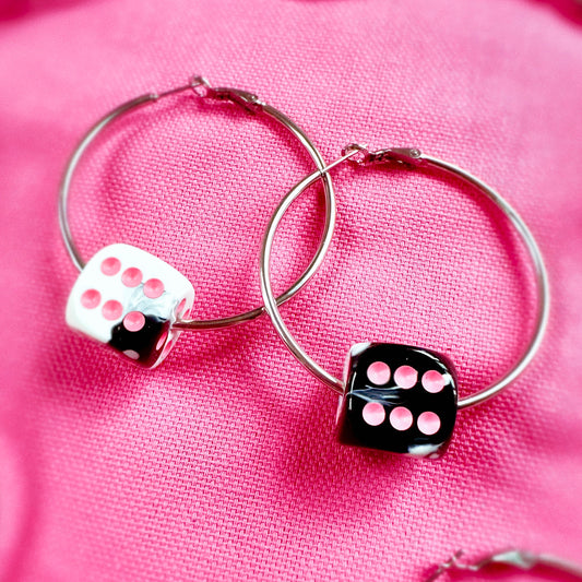 Hoop earrings with dice charms on a pink fabric background