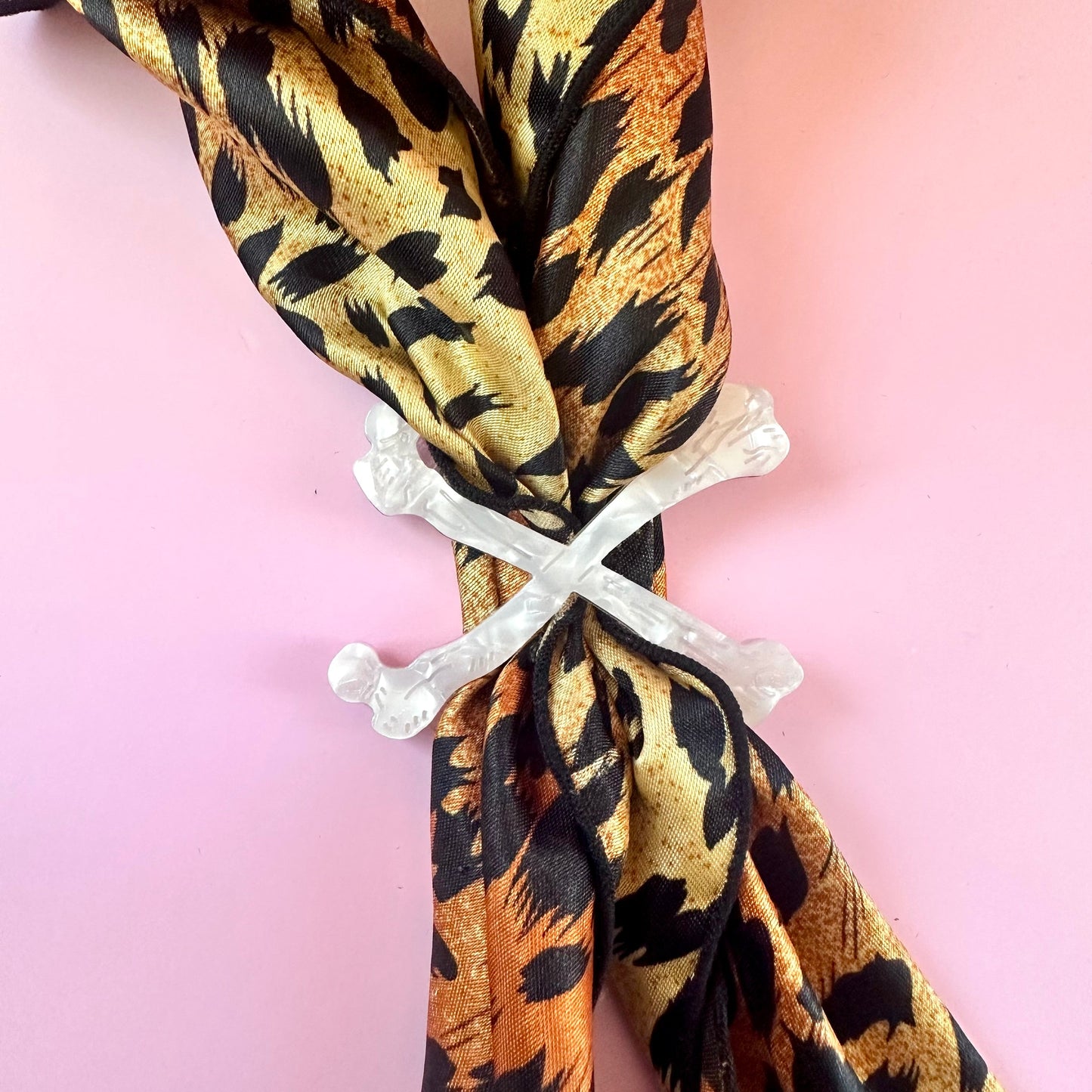 white crossbones scarf ring on leopard print scarf on pink background