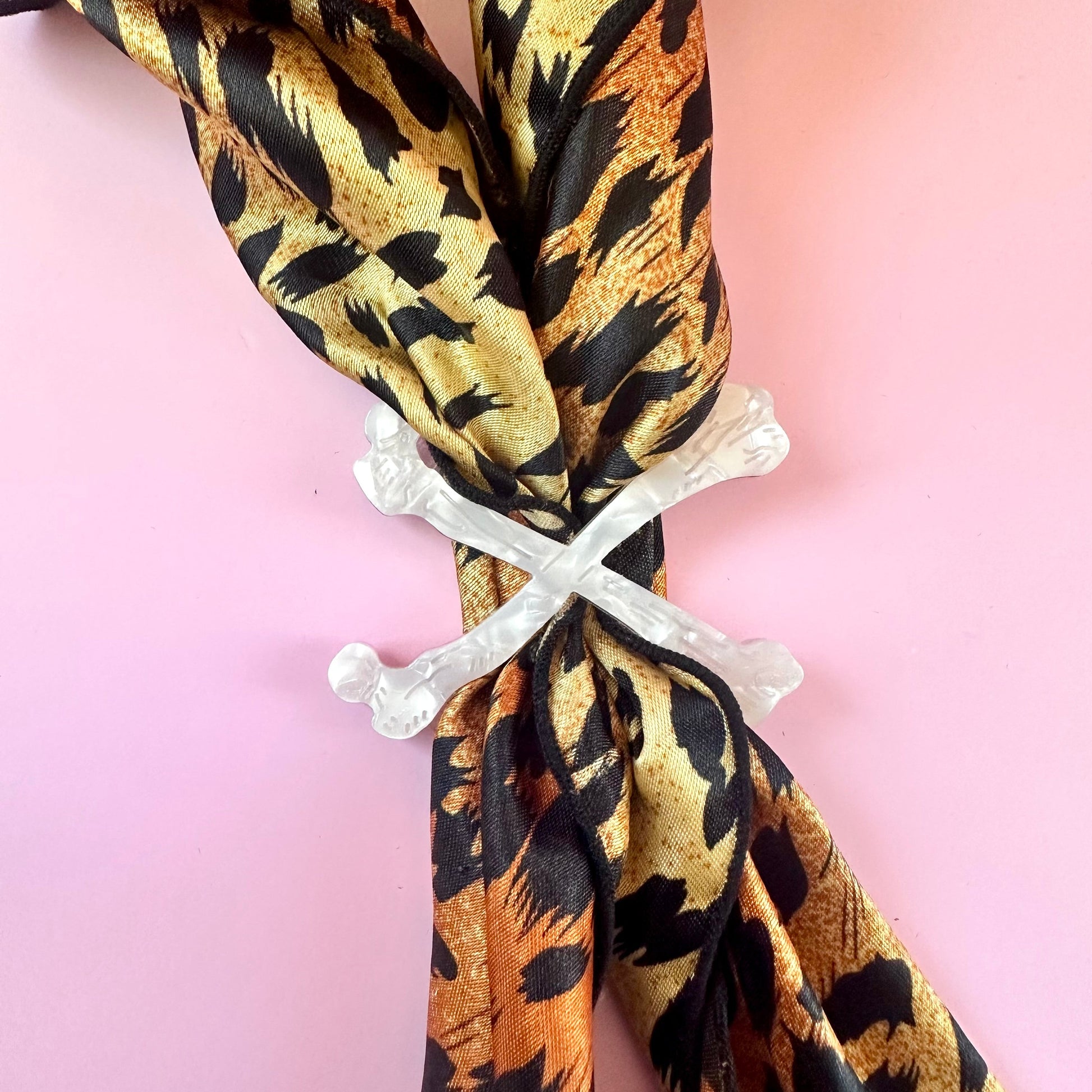 white crossbones scarf ring on leopard print scarf on pink background