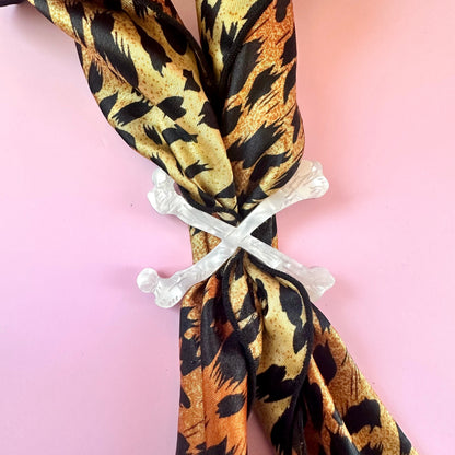 white crossbones scarf ring on leopard print scarf on pink background