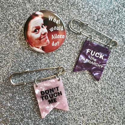 two safety pin banner pins in pink and purple that say Fuck the Patriarchy and Don't touch me. Plus a button pin of Aileen Wournos that says "What would Aileen do?"