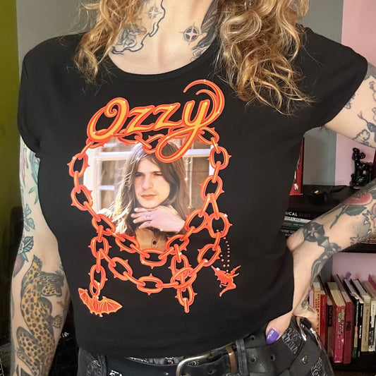 Person wearing a black t-shirt with orange graphics and text, standing indoors.