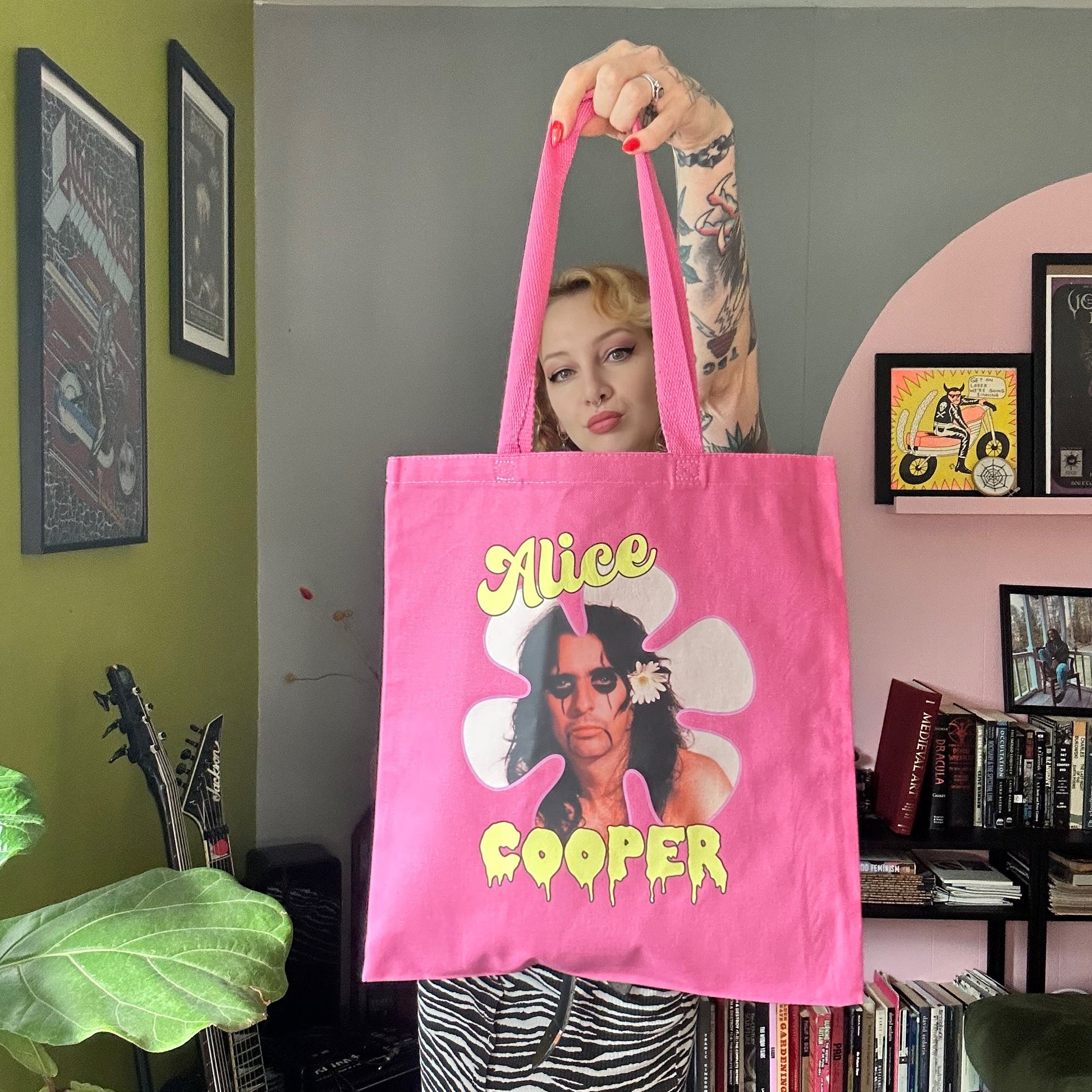 Person holding a pink tote bag with 'Alice Cooper' design in a room.