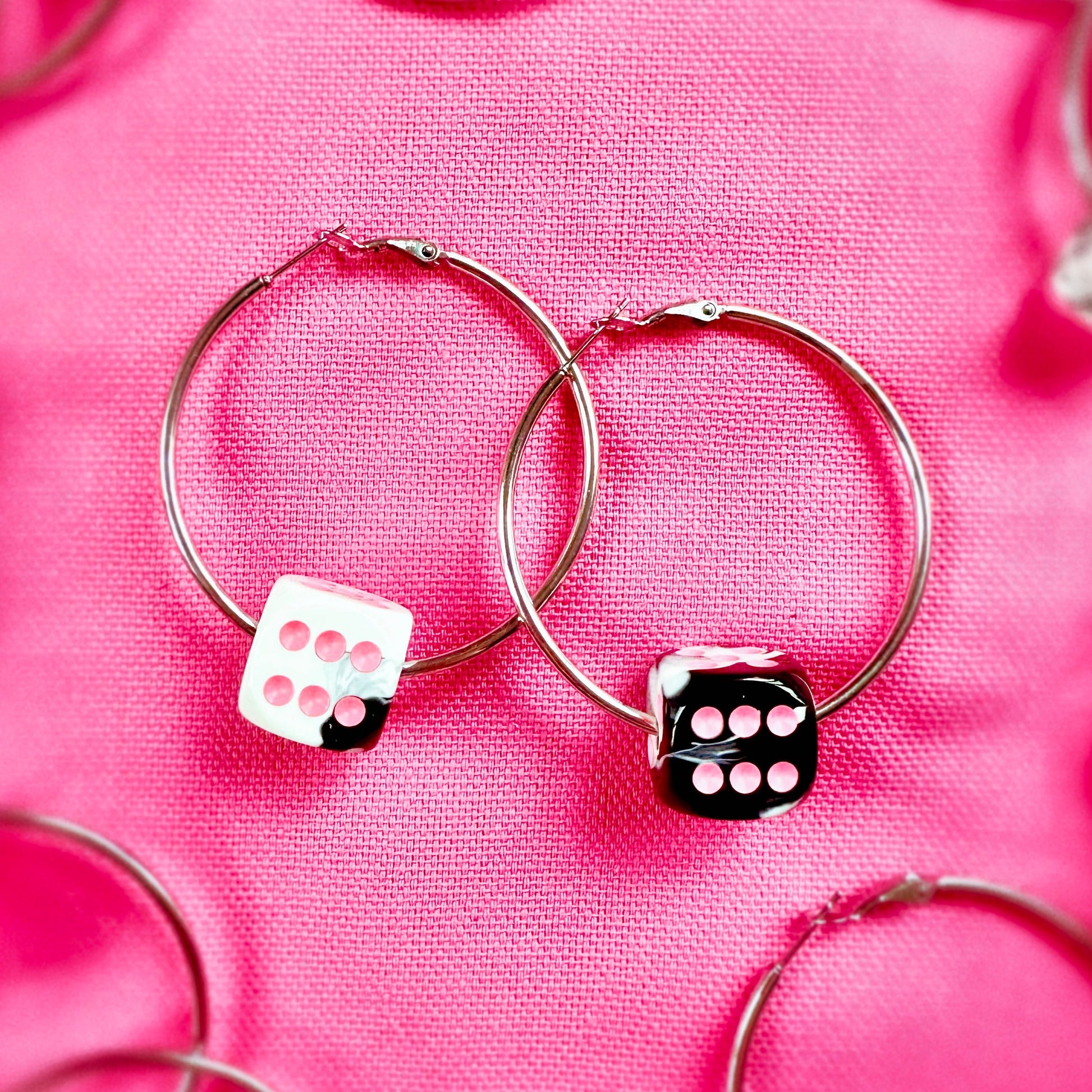 Silver hoop earrings with dice-shaped charms on a pink fabric background