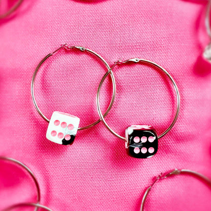 Silver hoop earrings with dice-shaped charms on a pink fabric background