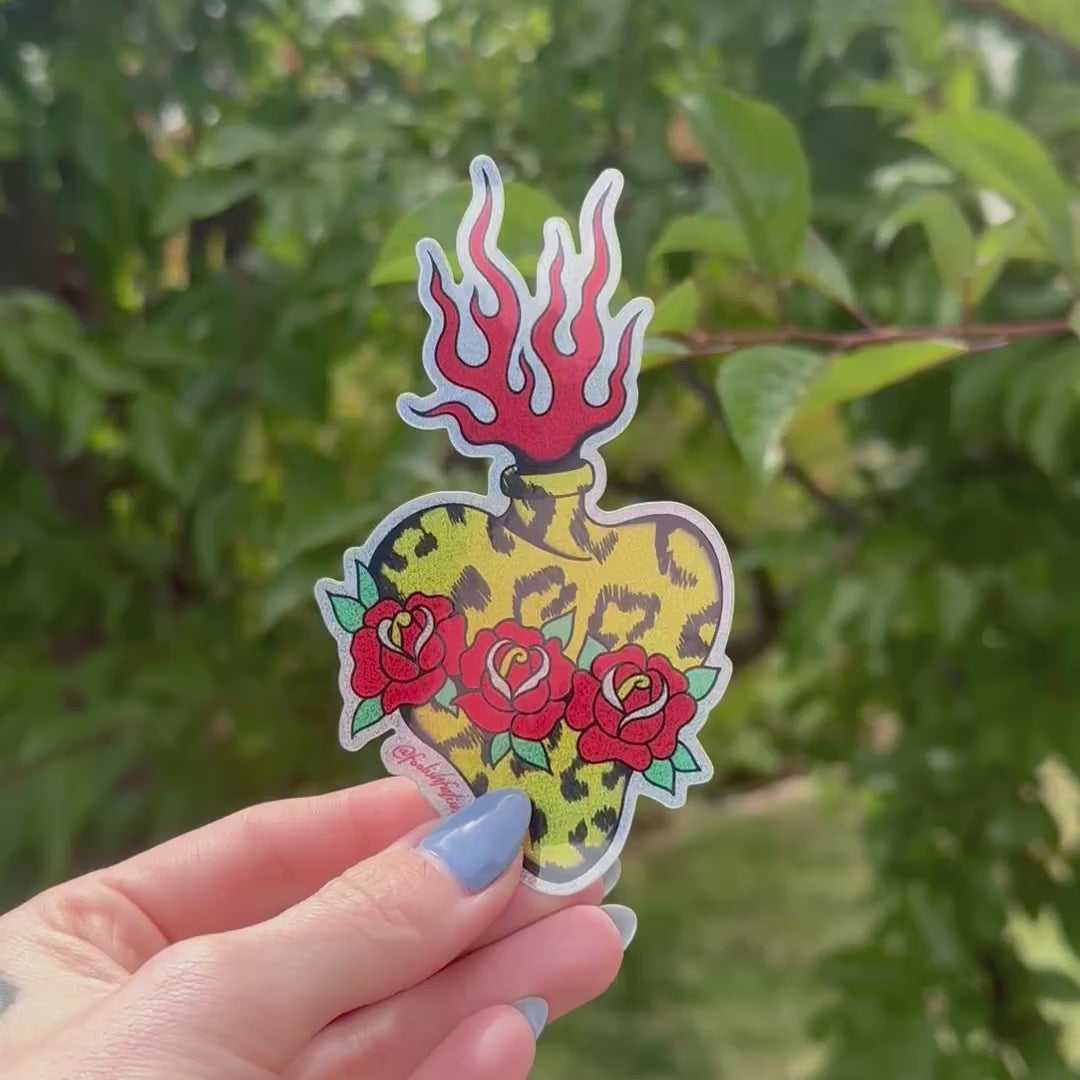 video of a yellow leopard print sacred heart stickers that has 3 red roses and red flames against a green tree background