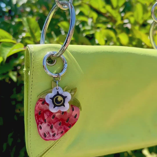 video of a strawberry bag charm on a lime green purse handbag with trees in background