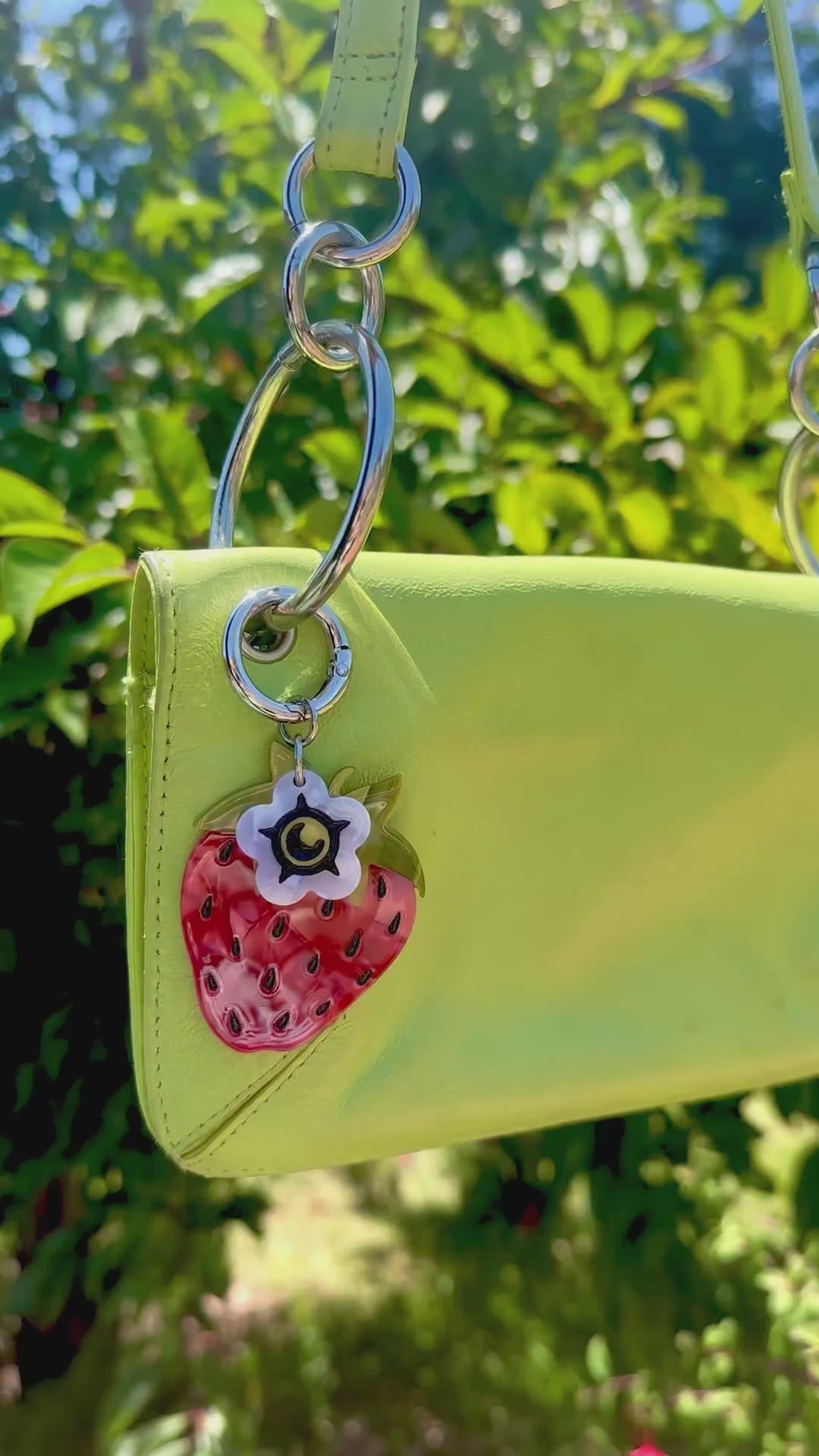 video of a strawberry bag charm on a lime green purse handbag with trees in background