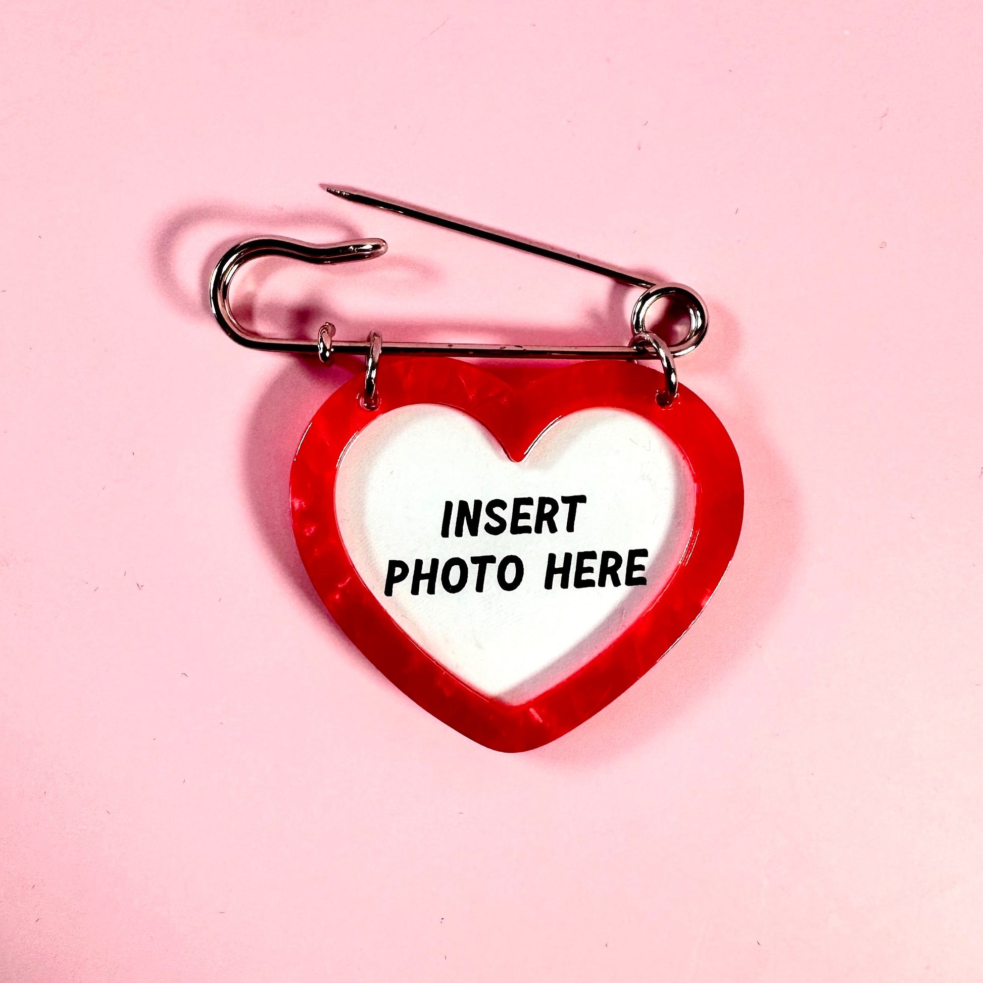 Red heart-shaped photo frame with a safety pin on a pink background