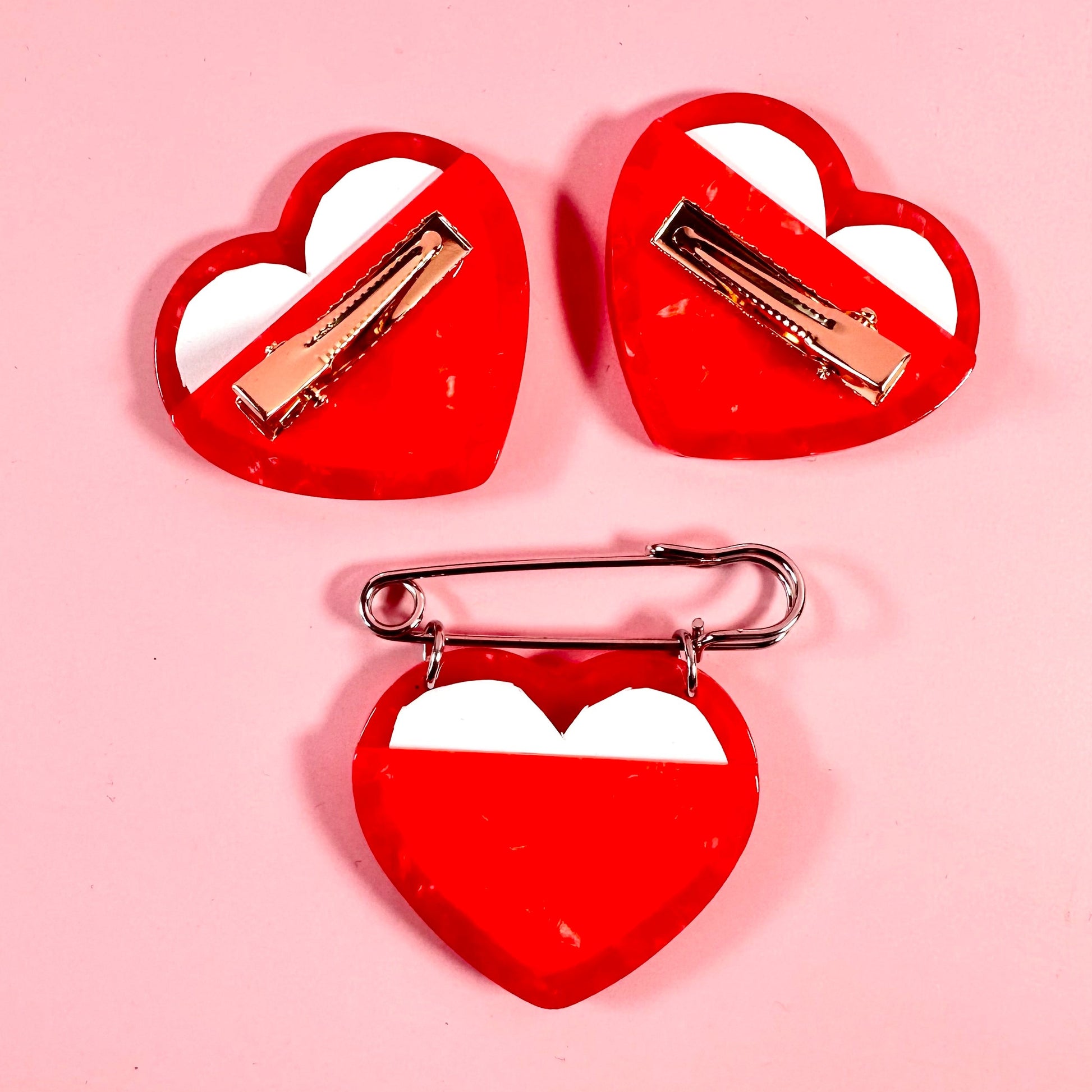 Three red heart-shaped hair clips with white centers on a pink background