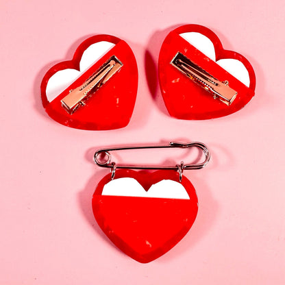 Three red heart-shaped hair clips with white centers on a pink background
