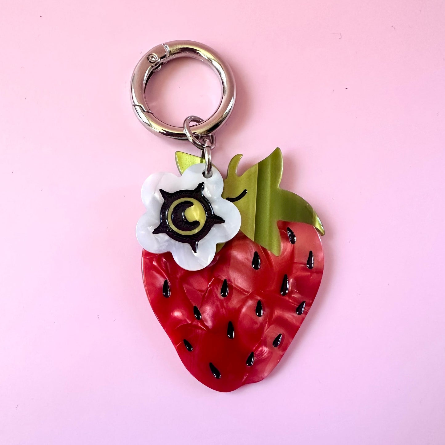 red strawberry bag charm with small white flower blossom charm on pink background