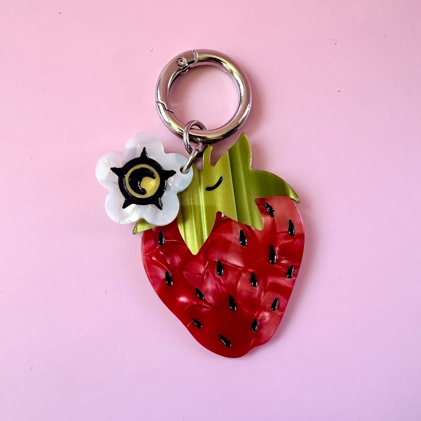 red strawberry bag charm with small white flower blossom charm on pink background