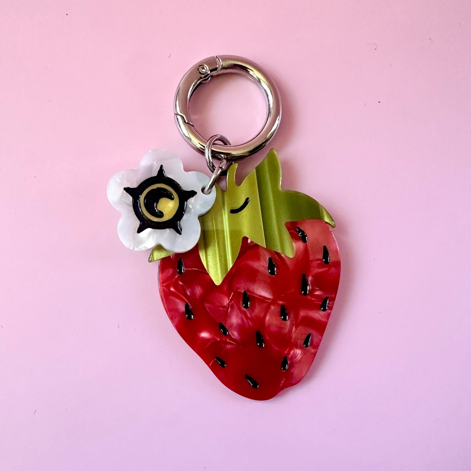 red strawberry bag charm with small white flower blossom charm on pink background