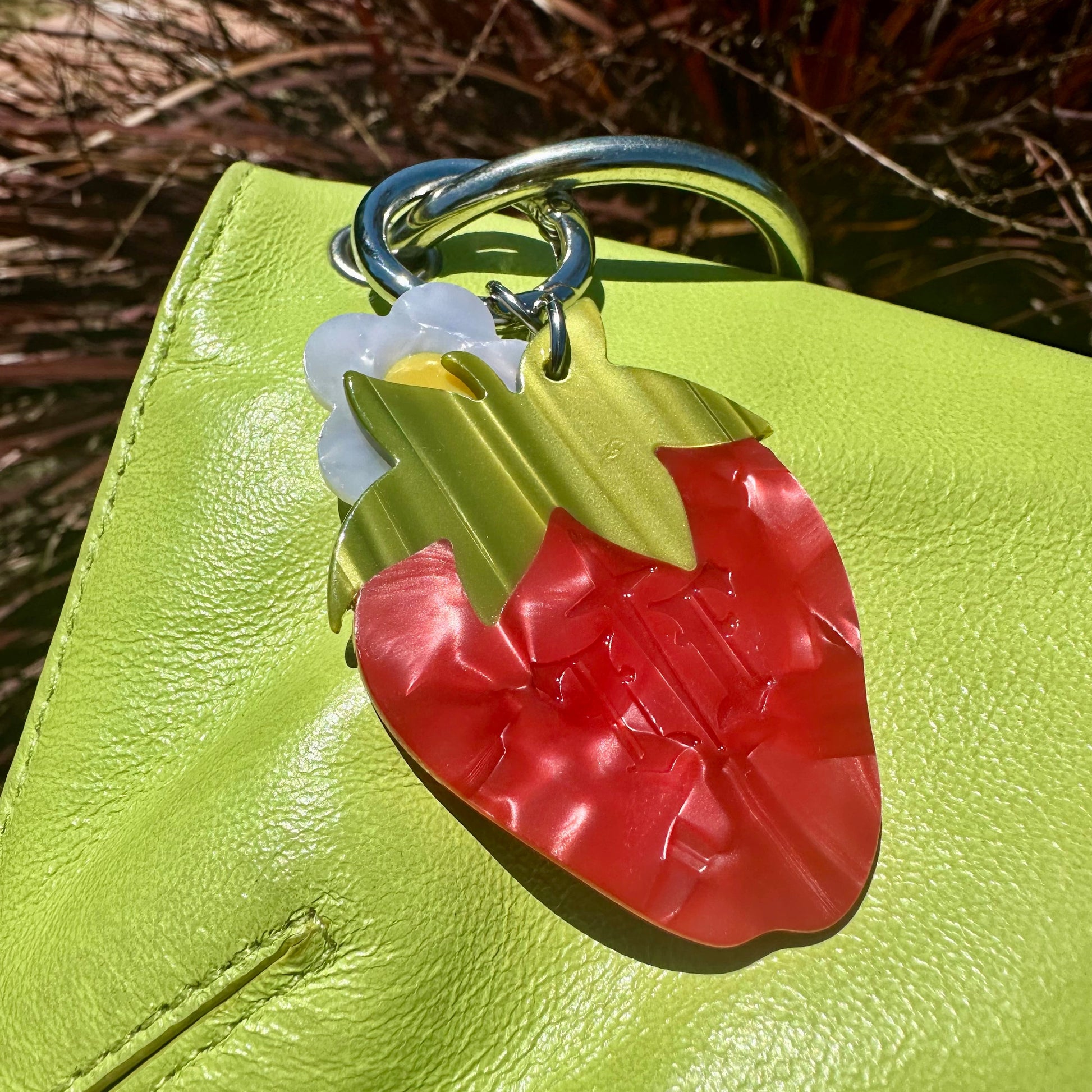 The back of the red strawberry bag charm with small white flower blossom charm on a lime green purse