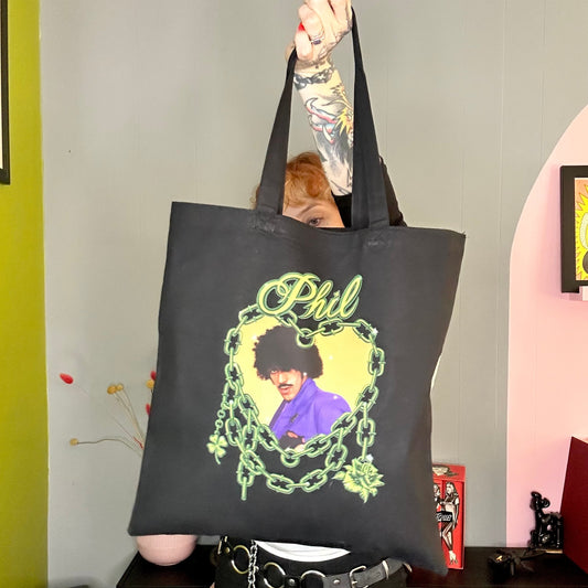 Person holding a black tote bag with a graphic design of a person in a purple outfit and text.
