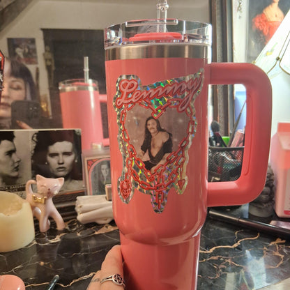 Pink tumbler with decorative design held in a hand against a cluttered background