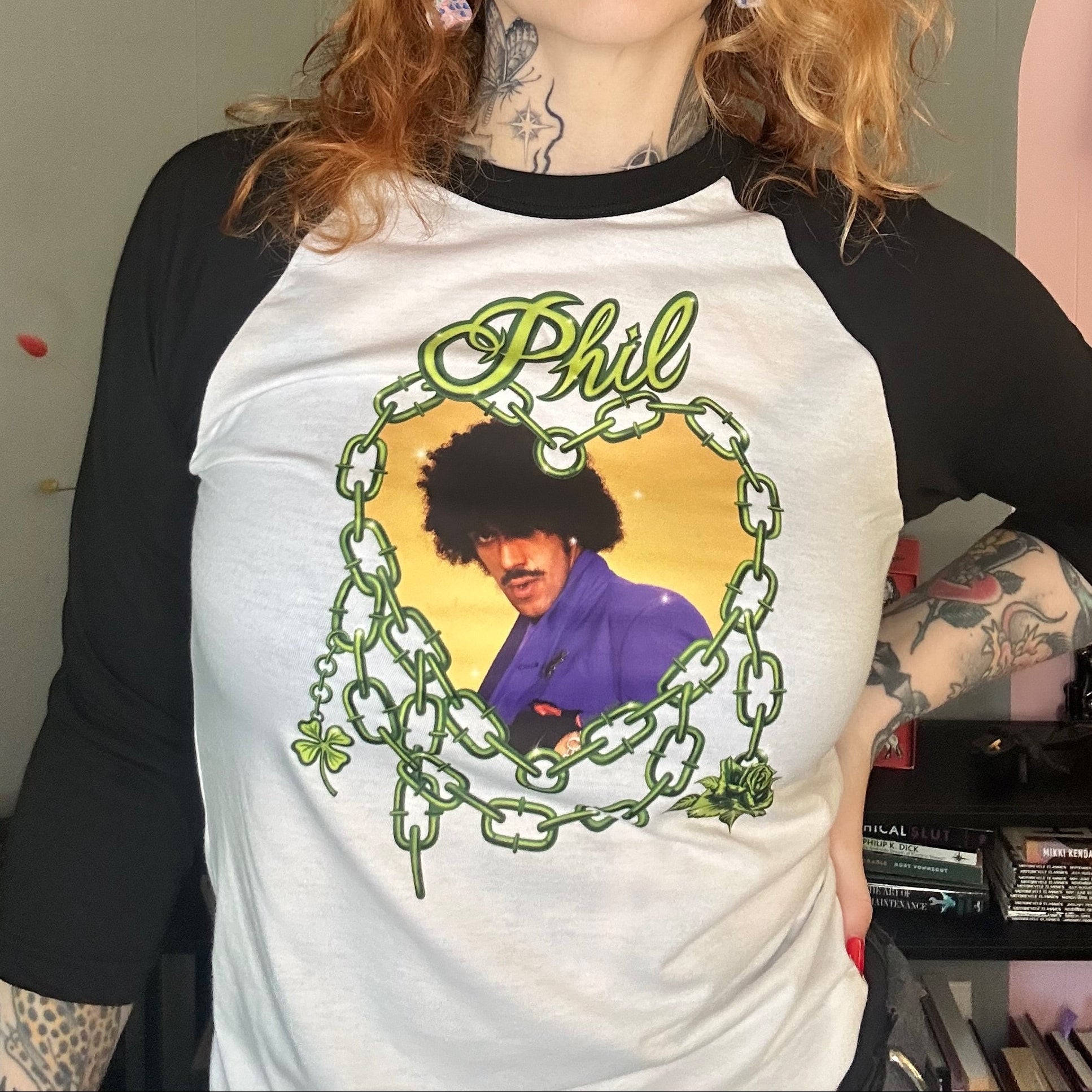 Person wearing a t-shirt with a graphic design of a person with curly hair and text, in an indoor setting.