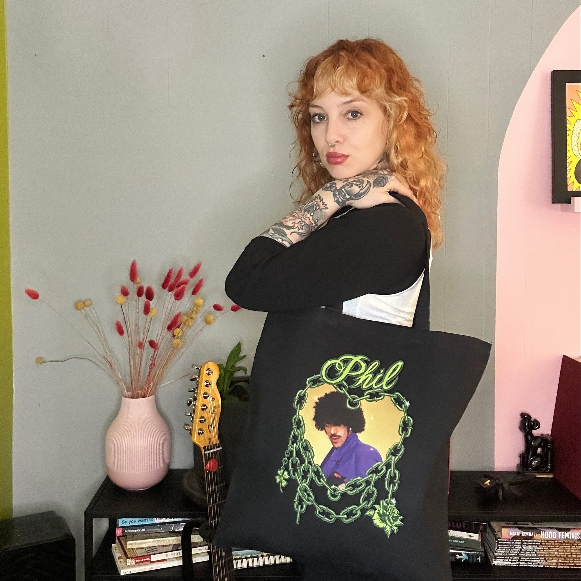 Person holding a pillow with a graphic design in a room with a guitar and books.